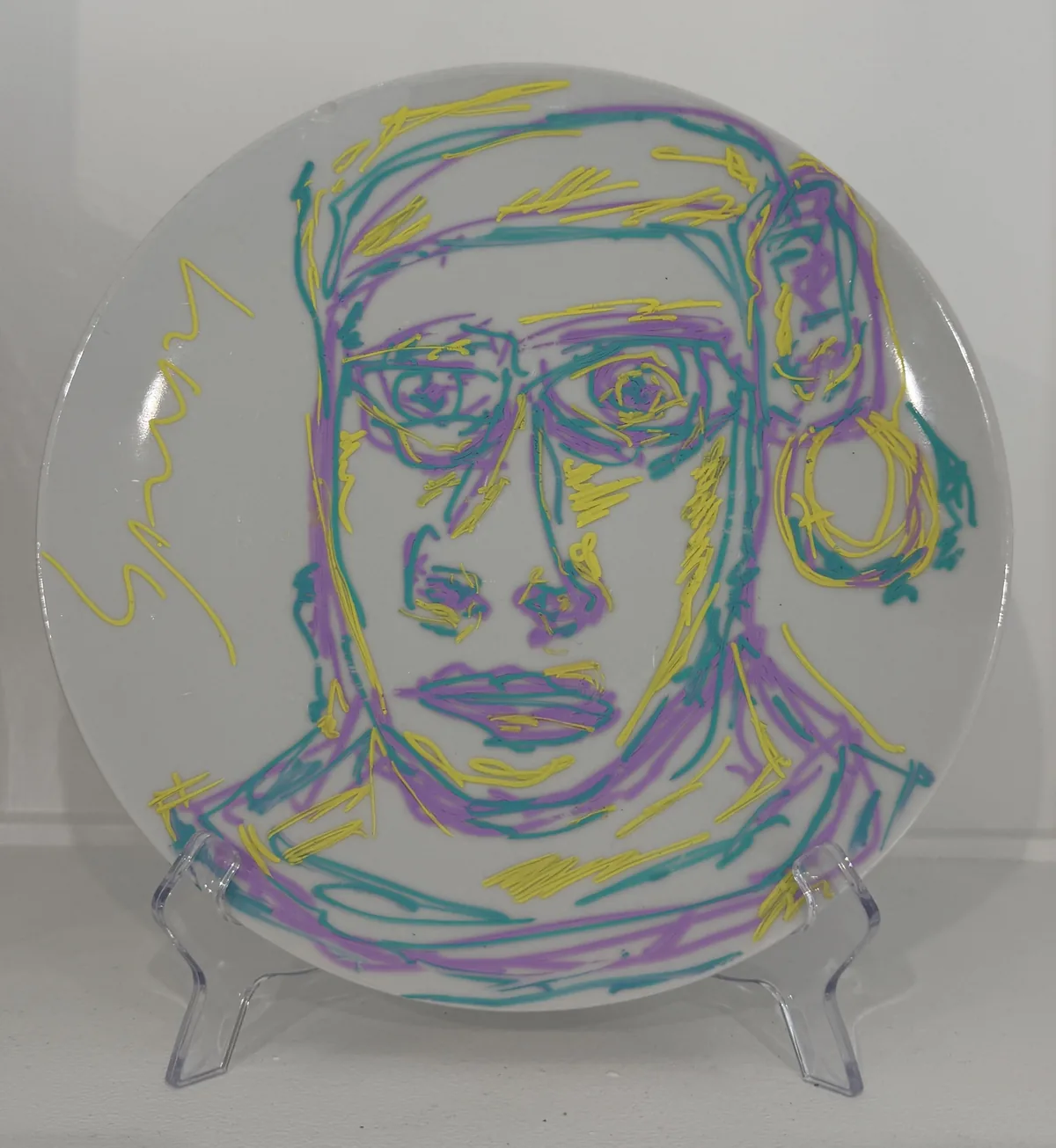 Ceramic no. 11: a white plate with a face drawn in one continuous raised line, yellow, turquoise and violet