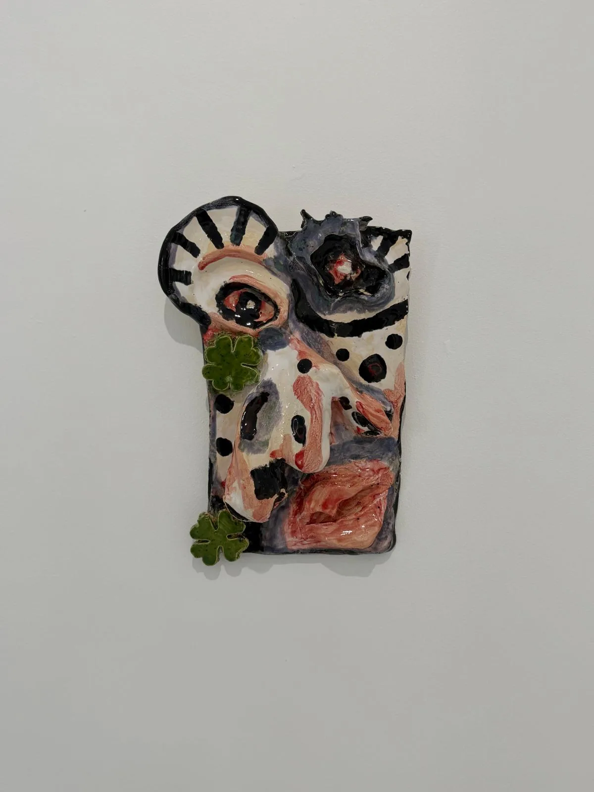 Ceramic no. 2: a face in high relief on a plaque, pink and cream glaze, two green four-leaf clovers breaking out of the edge