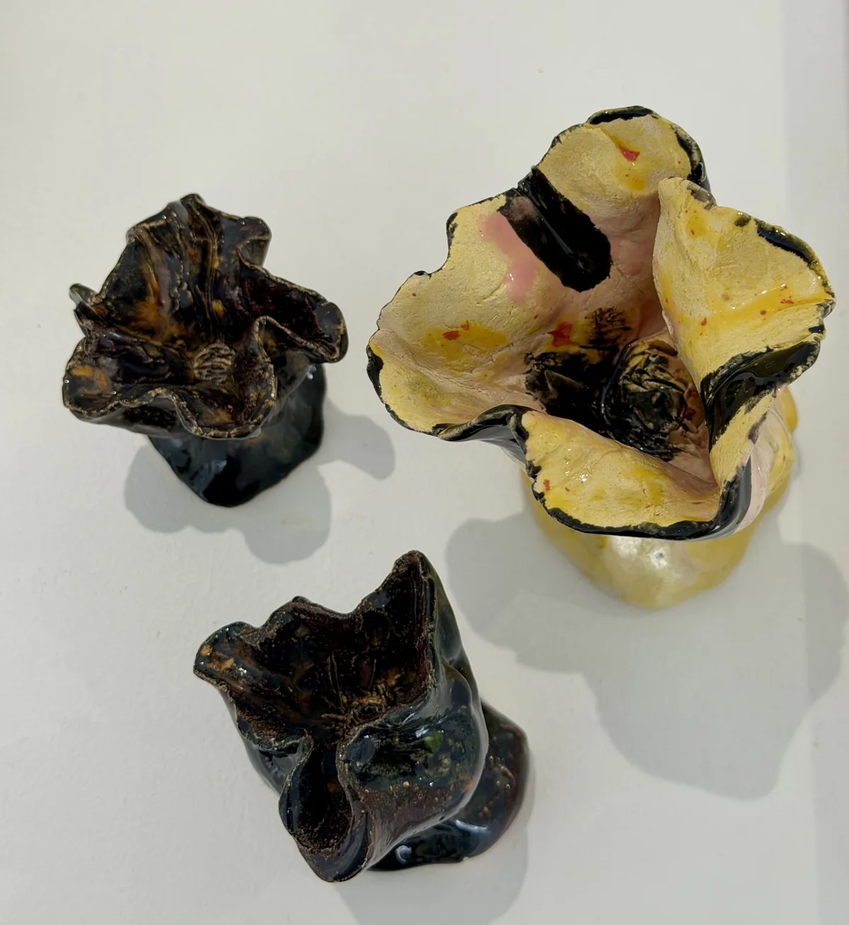 Ceramic no. 6: three ceramic flowers on short feet, two dark brown and glossy, one pale yellow with pink and red