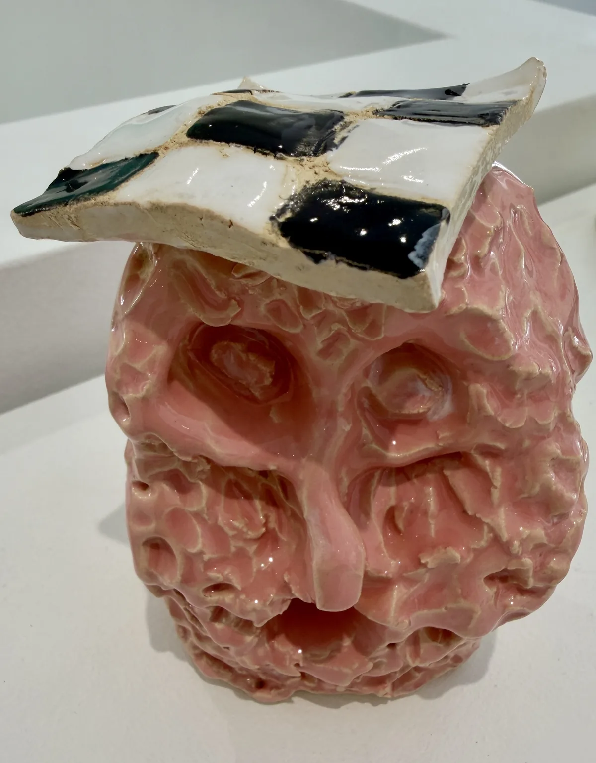Ceramic no. 7: an ovoid pink head full of hollows, topped with a black and white checkerboard plate