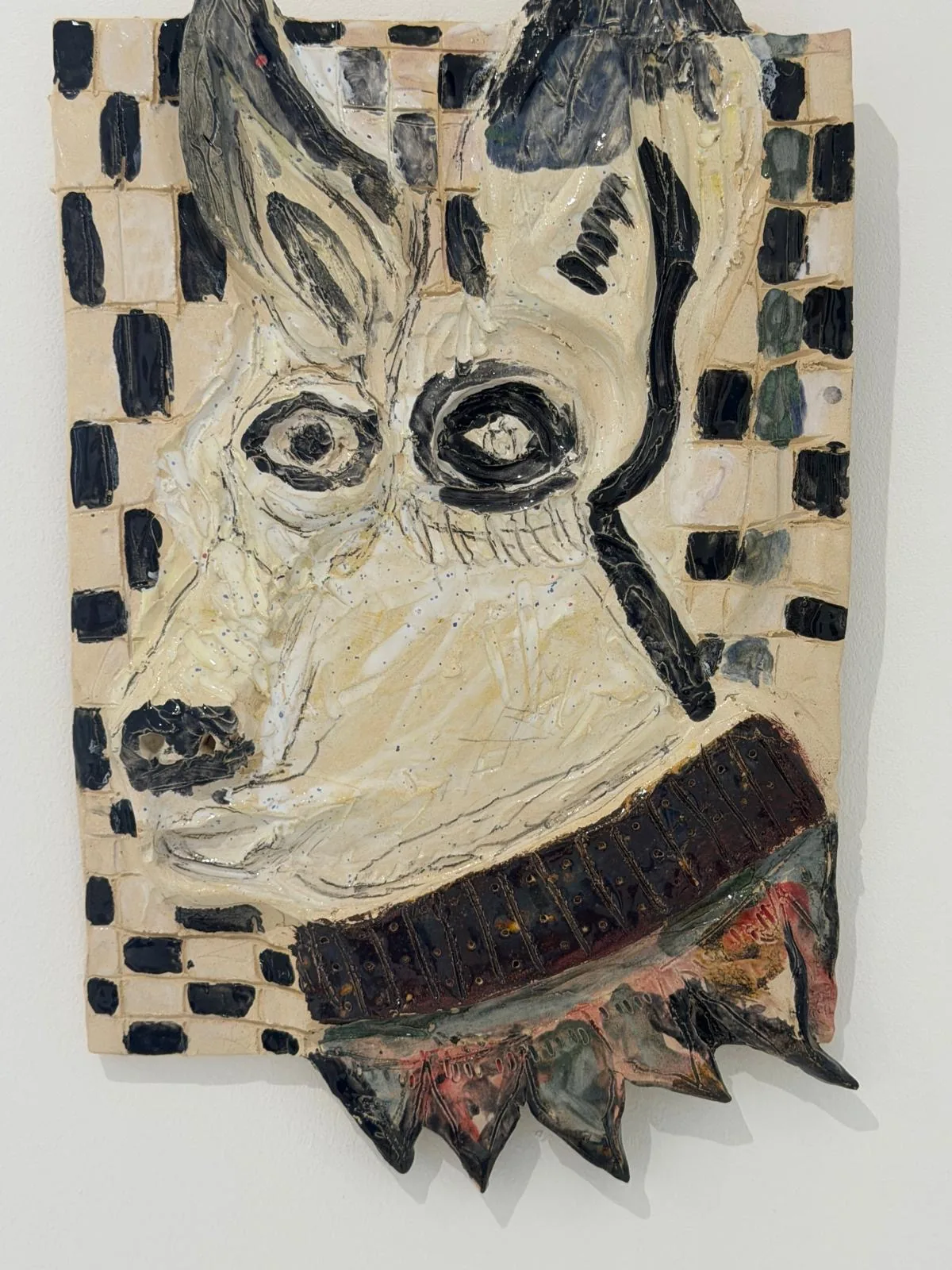 Ceramic no. 1, the Dog: a ceramic wall relief of a pointed-eared animal head, cream glaze, black checkered border and a spiked collar