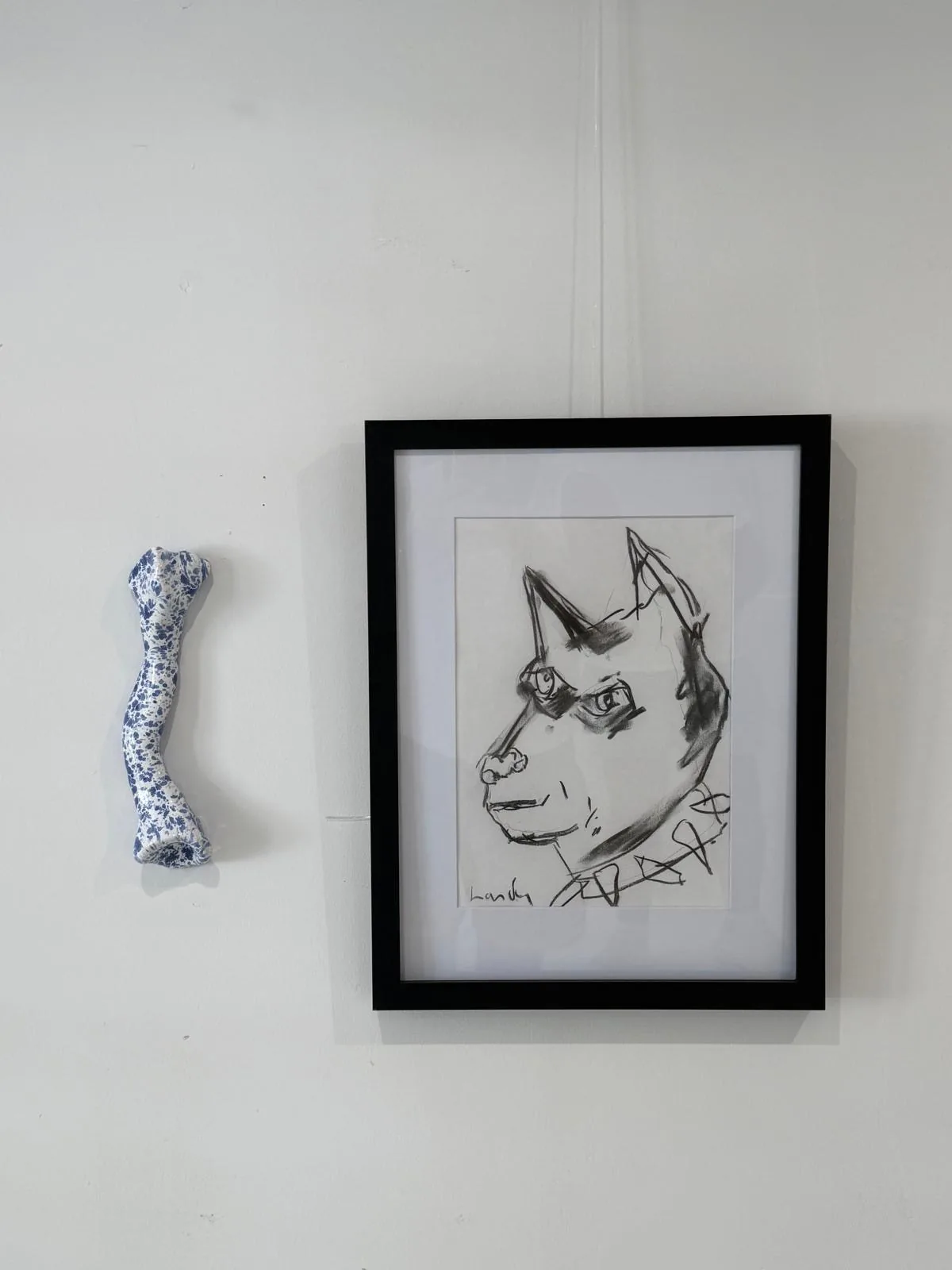 Le chien: a framed black ink drawing of a growling dog with a spiked collar, hung beside a blue-speckled ceramic bone