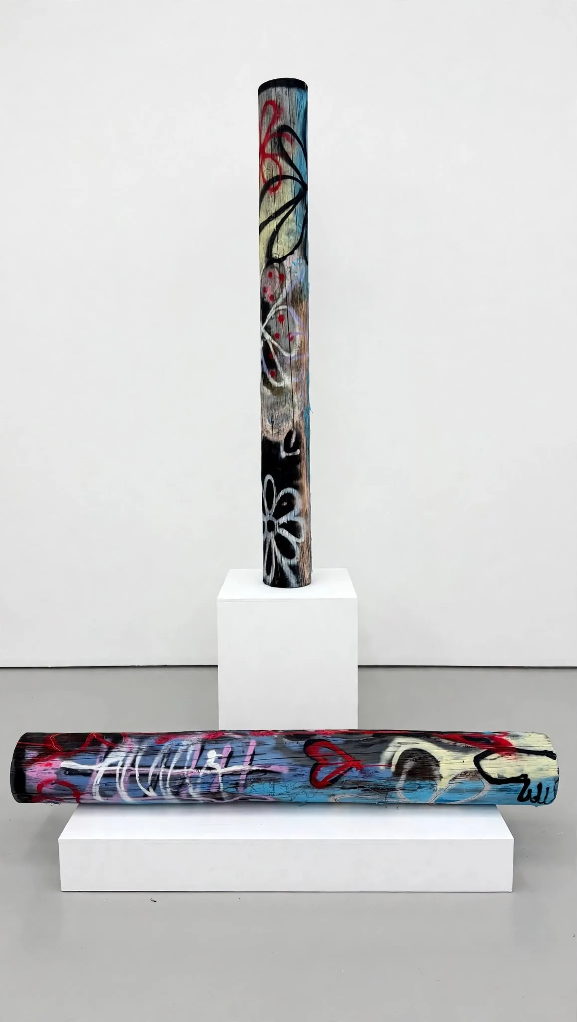 Two Totems: one standing on a white cube, one lying on a low plinth